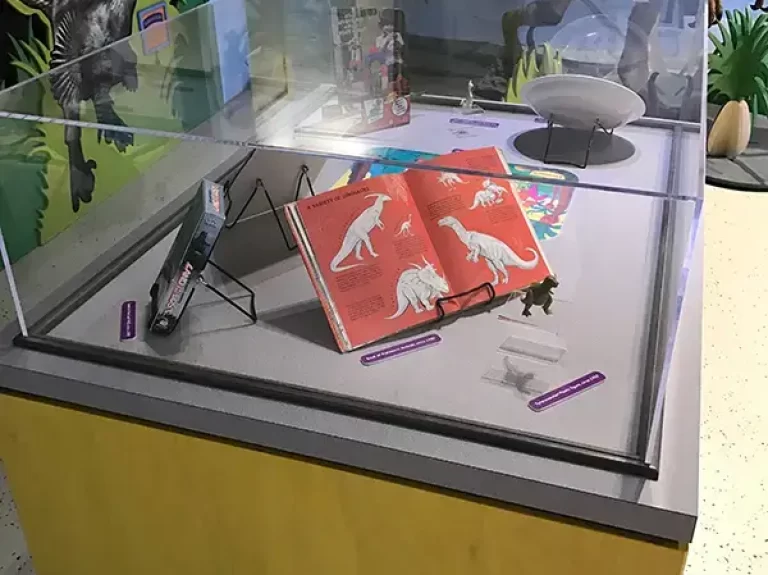 A display case filled with books, toys, and pop culture items about dinosaurs.